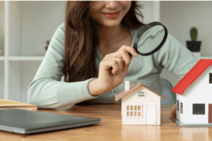 A woman looking at a model house through a magnifying glass.