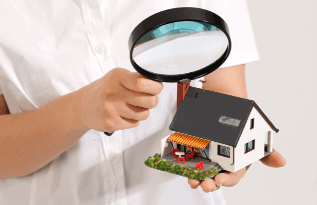 A person holding a magnifying glass over a house.