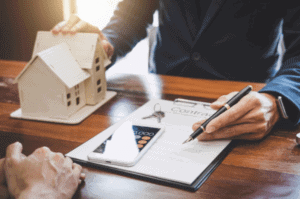 A person is writing on paper with a house and keys.