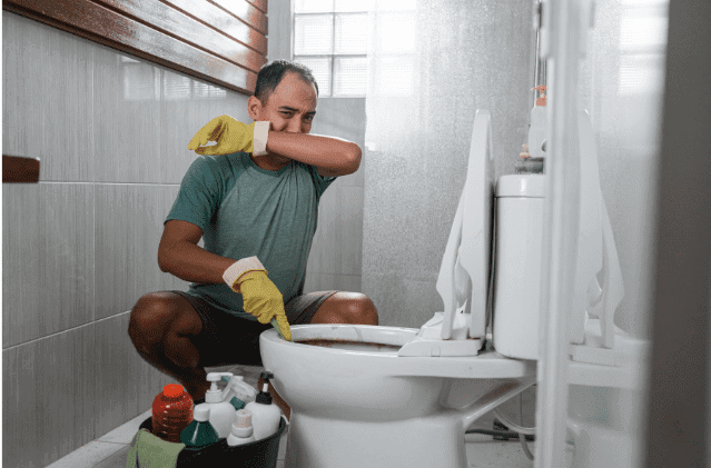 A man in the bathroom cleaning his toilet.
